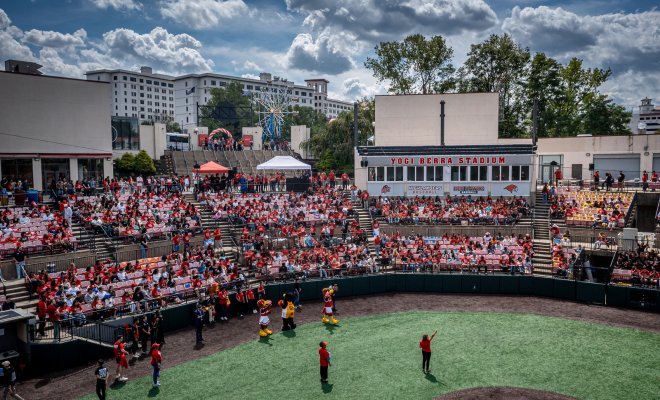 A large crowd of students fills the stands at Yogi Berra Stadium during a Weeks of Welcome event featuring mascots and activities on the field.