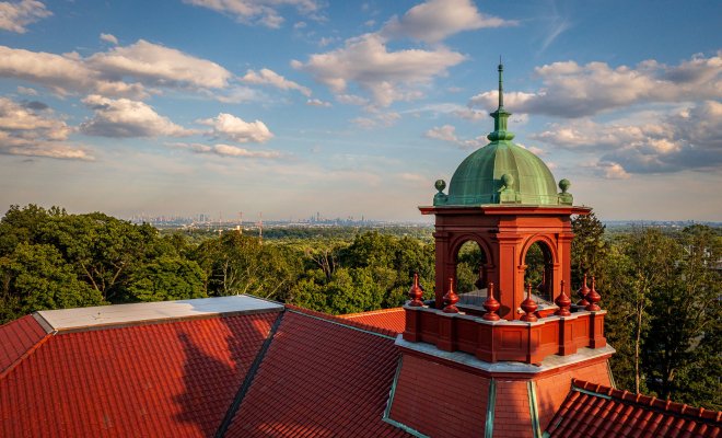 ariel view of the red rooftop and green dome of Cole Hall building with NYC in skyline