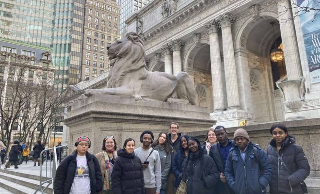A group of college students pose in front of the Lion Statues in front of the New York Public Library