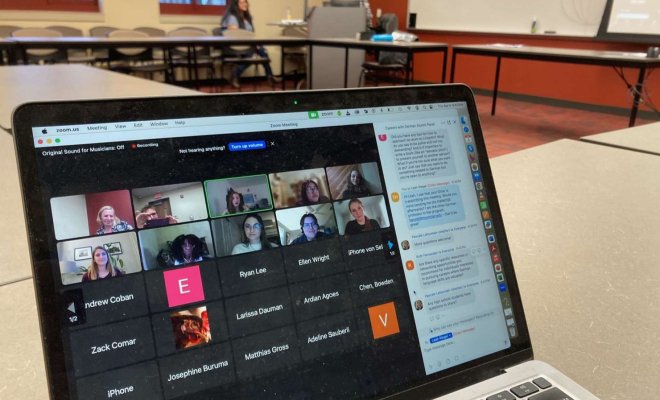 A laptop sits on a table and a Zoom call displays on the screen