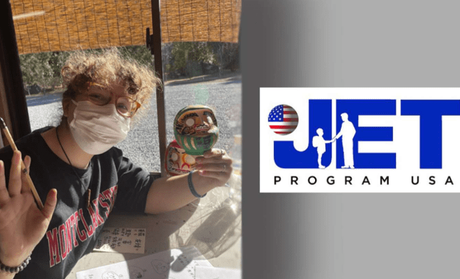A woman wears a facemask and holds a painted carving  