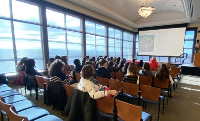 A group of people sit in a conference room and watch a presentation