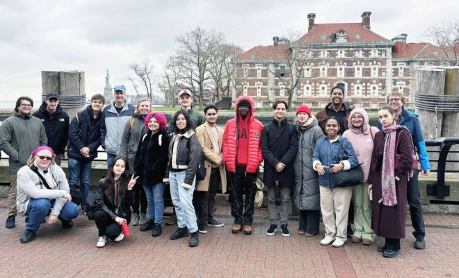 A group of college students and professors pose in front of Ellis Island