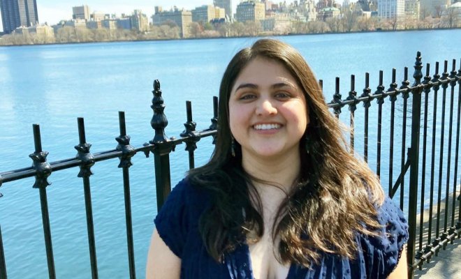 A woman stands in front of a wrought iron fence in front of a lake