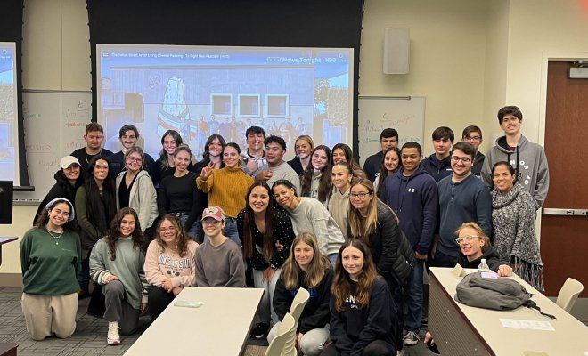 A group of college students pose in a classroom in front of a projector screen