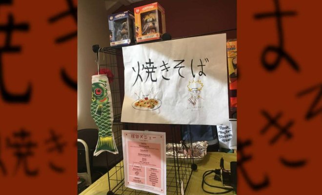 Japanese food booth display with a hand-drawn “焼きそば” (yakisoba) sign, menu, carp streamer, and anime-themed decorations