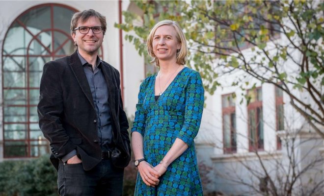 Two adults pose for a headshot outside in front of a building