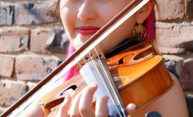 A woman holds a violin and smiles at the camera