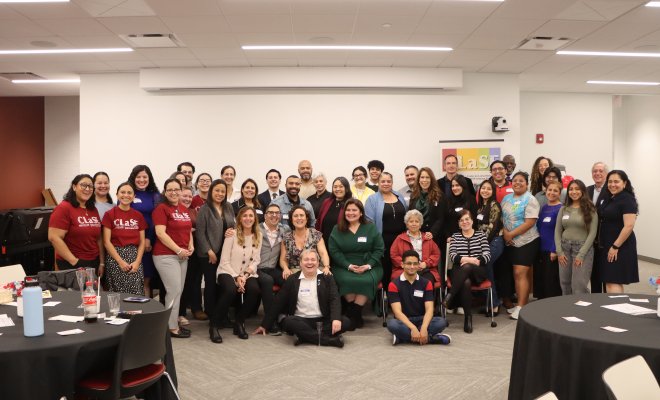 A group of people pose inside a conference room, a few wear t-shirts that read "Clase"