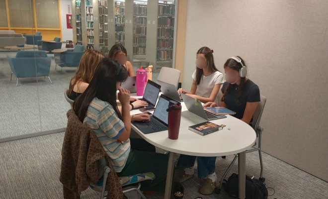 5 students sitting at a table on laptops inside a study pod