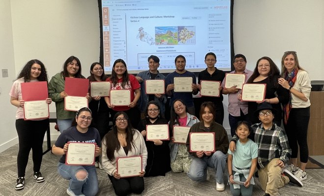 A group of people pose in two lines in front of a projector screen, nearly everyone holds up a framed paper certificate