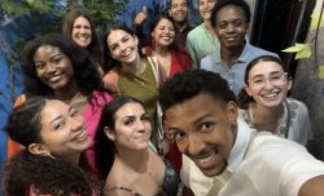 A college student holds a phone and takes a selfie with a group of other college students