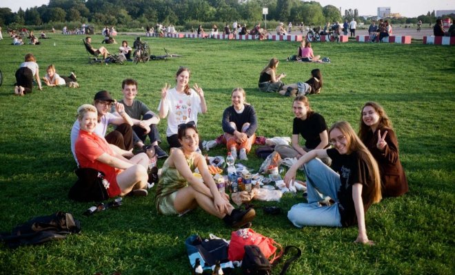 A group of college students sit on the grass in a circle in a large field