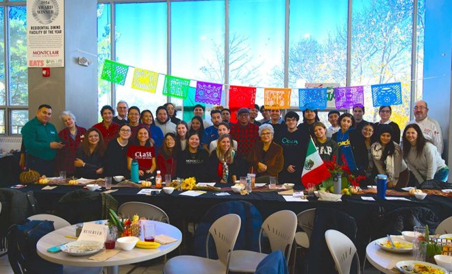 A large group of people pose together in a room with large windows and colorful flags
