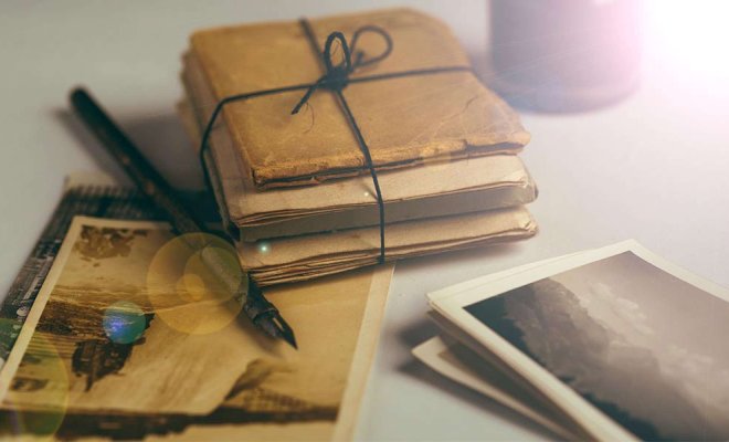 A stack of aged letters tied with string rests beside a fountain pen and scattered vintage photographs on a softly lit desk
