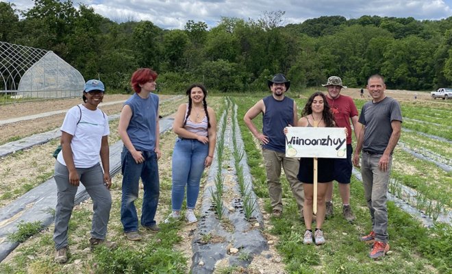 A group of people stand in the middle of a crop field while one holds a sign
