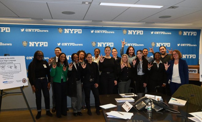A group of people pose inside a conference room in front of a banner with the NYPD logo