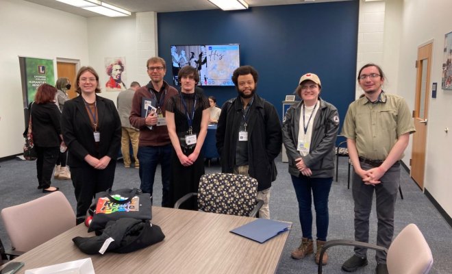 A group of college students stand inside a classroom and pose for a photo
