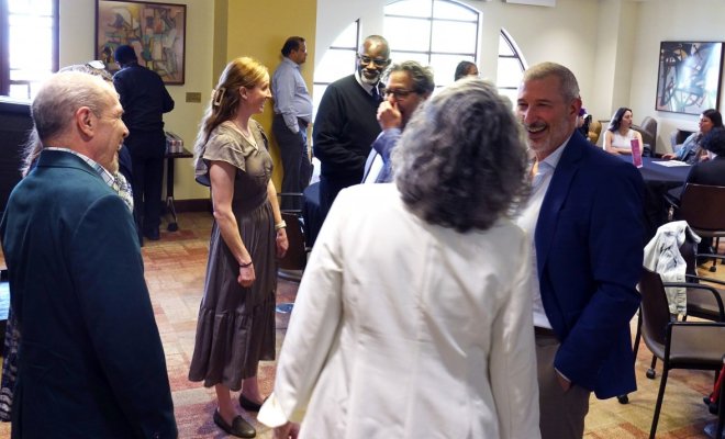 A gorup of people in professional attire mingle inside a conference room