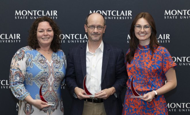 Three people wear professional attire and pose together, each holding a glass award
