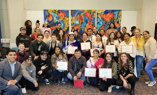 A large group of college students, some holding paper certificates, pose in front of an art installation