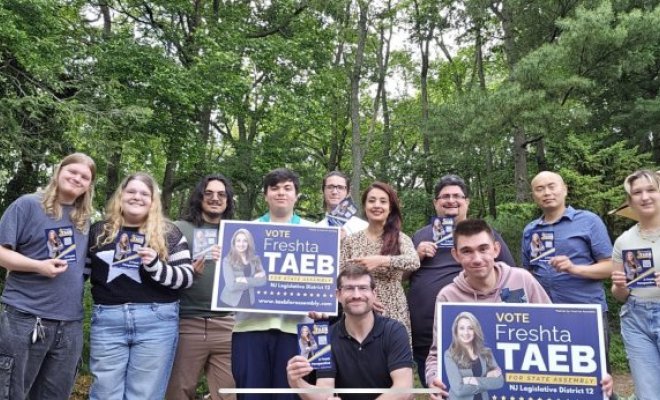 A group of people stand together holding signs reading "Vote Freshta Taeb"