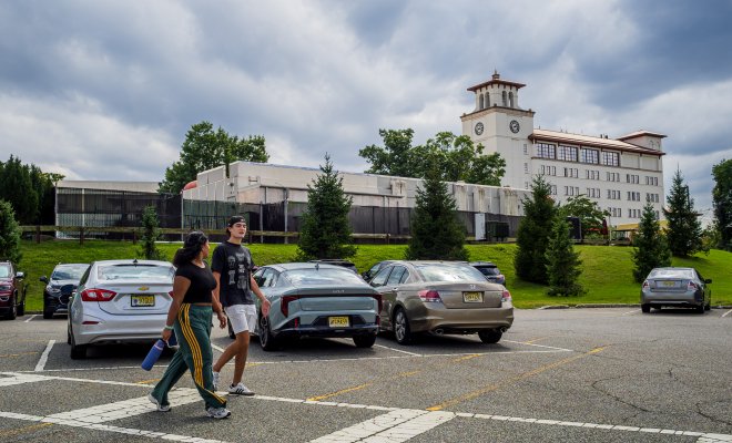 two students walking on a cross walk with a car in the background