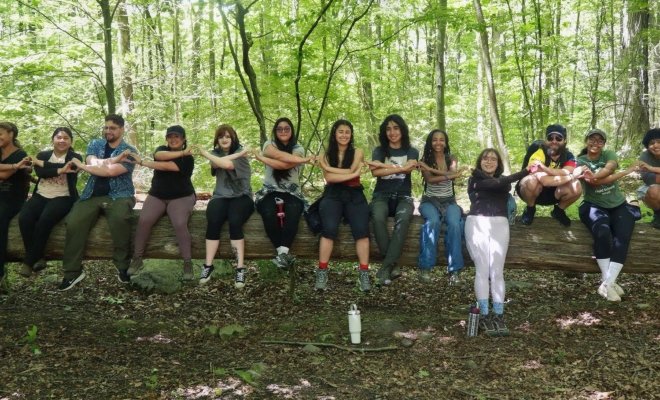 photo of field school students sitting on a fallen tree log, interlocking arms and using hands to make hearts