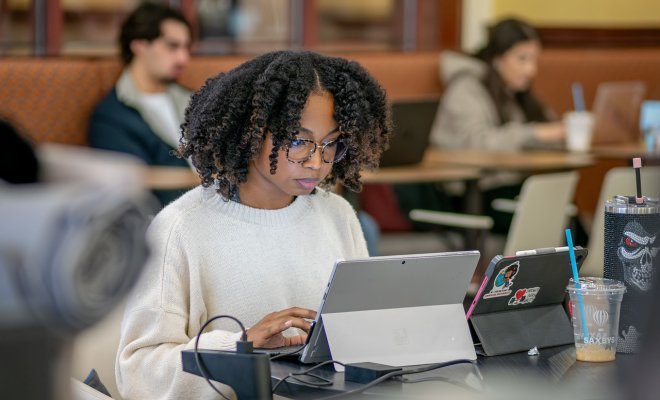 Female student sitting at a table working on a laptop and tablet ahead of finals.