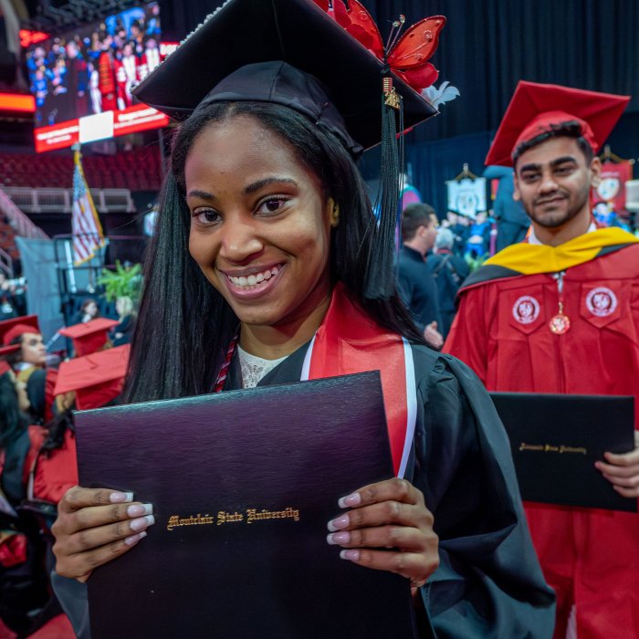 A graduate in a black gown proudly holds up her diploma.