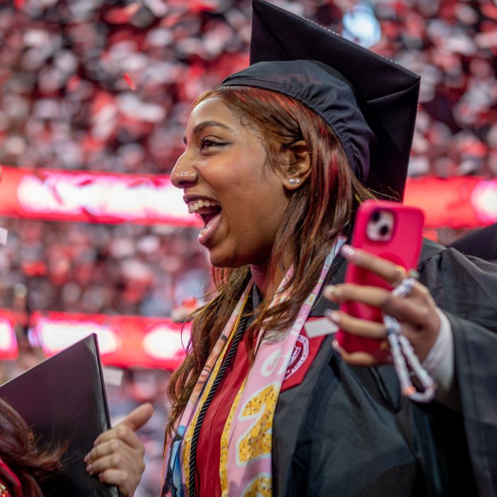 A graduate , holding a phone, expresses her excitement on the floor of the Prudential Center.