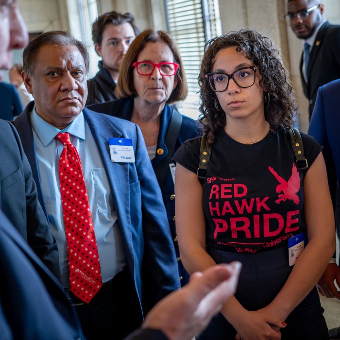 A woman wearing a Red Haw Pride t-shirt listens to a state senator.