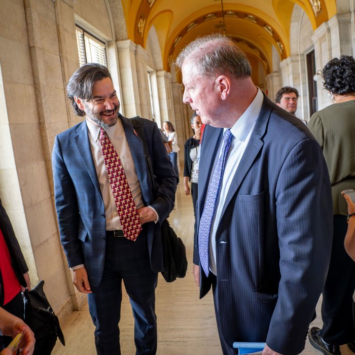 Two men smile in a hallway.