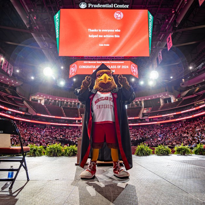 Rocky the Red Hawk on stage at prudential center with the jumbotron behind him.