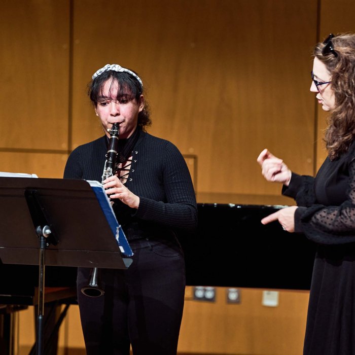 Female student plays clarinet for female teacher.