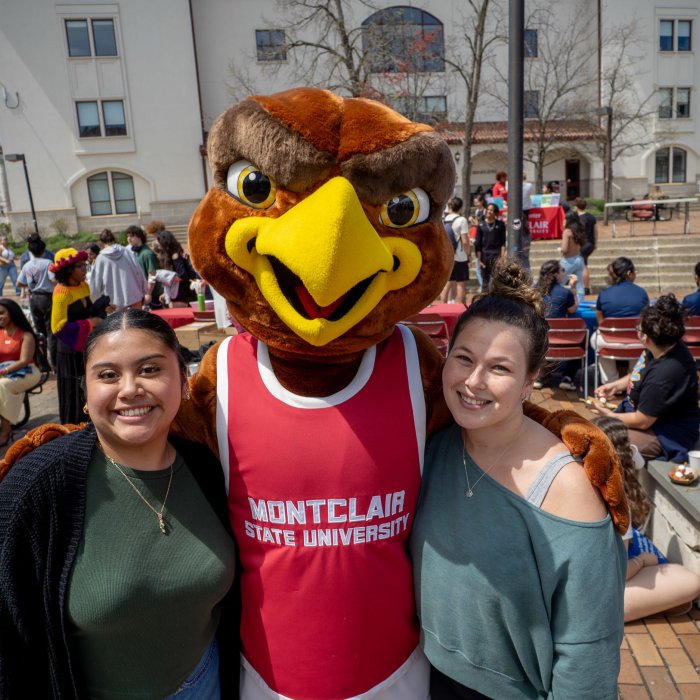 Two female presenting students with mascot Rocky.