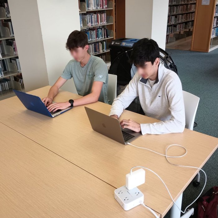 two students sitting at a desk on laptops