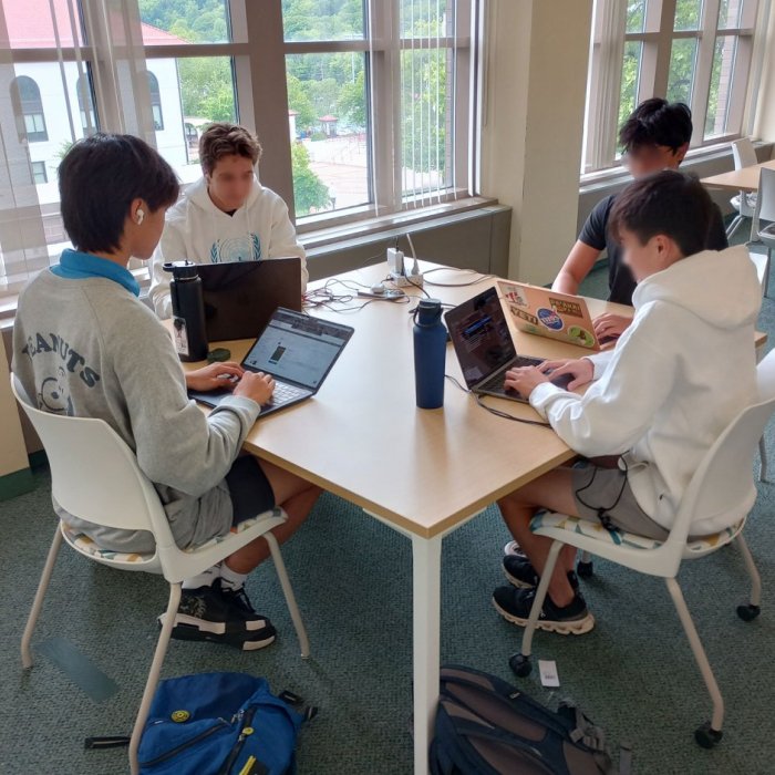 four students sitting at a desk on laptops