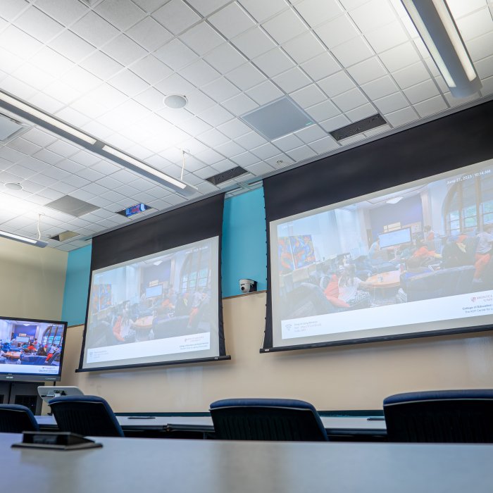 Empty table in front of two projector screens with image displayed 
