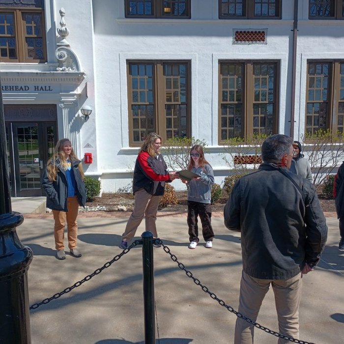 group standing in from of morehead hall with two people viewing a binder