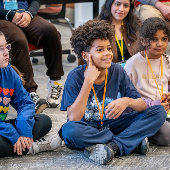 Children sit on the floor listening to somoene read a book