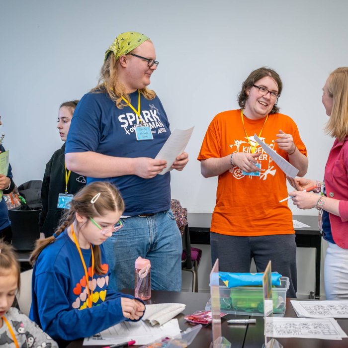 Three adults talk to eachother while children work on an activity at a desk