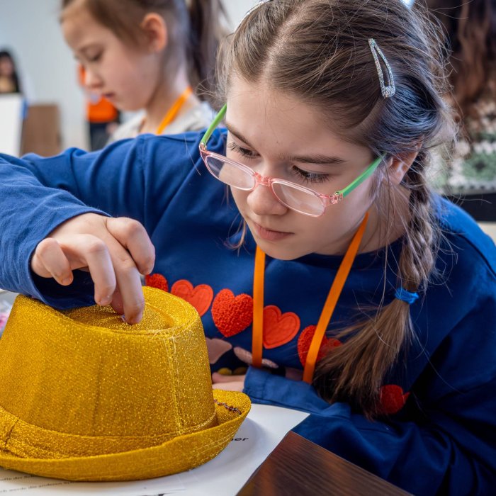 A young girl decorates a golden fedora 
