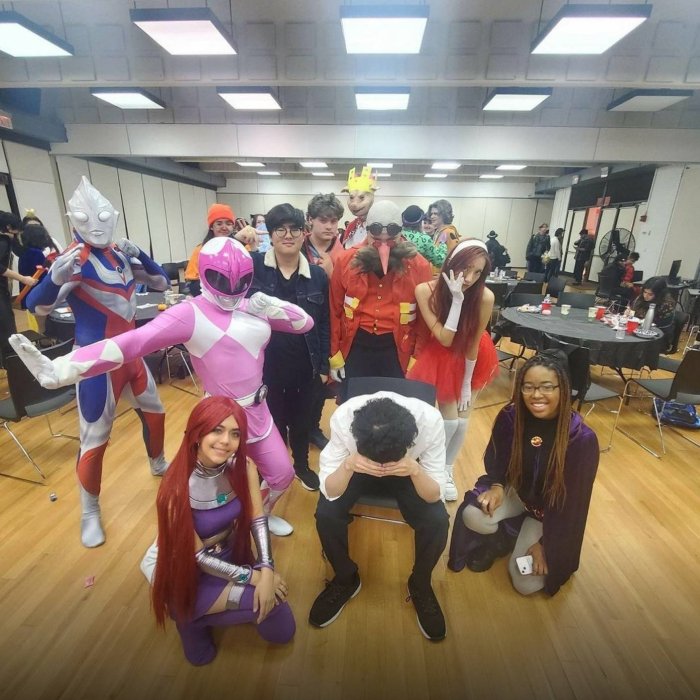 A group of about ten people wearing Halloween costumes pose together and smile at the camera