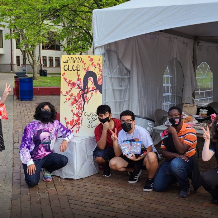 A group of six college students stand outside and wear face masks and pose in front of a sign that reads "Japan Club"