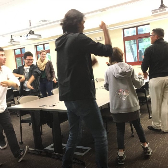 A group of college students walk around a table in a classroom