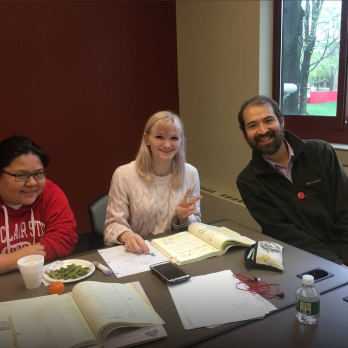 Three college students sit around a table with books with Japanese text spread out in front of them