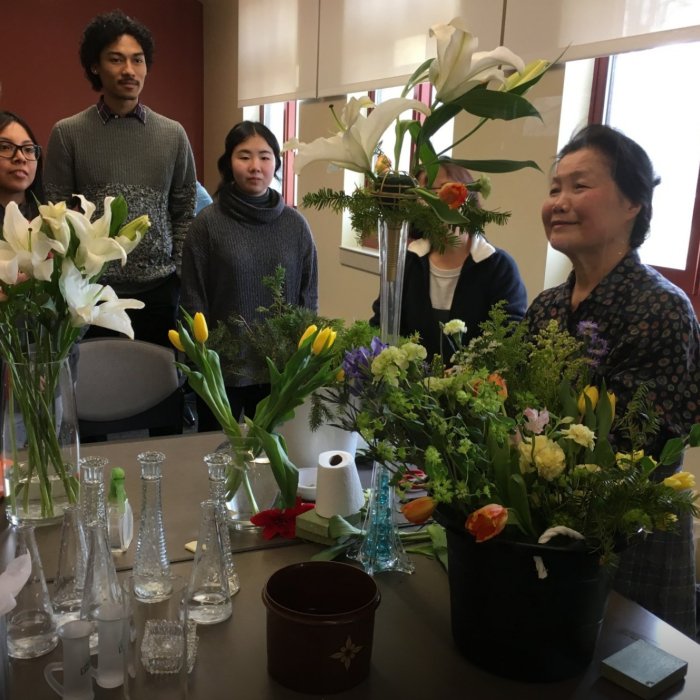 A group of people admires a large floral arrangement as a woman stands behind it