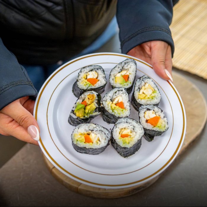 A person holds a plate of sushi rolls