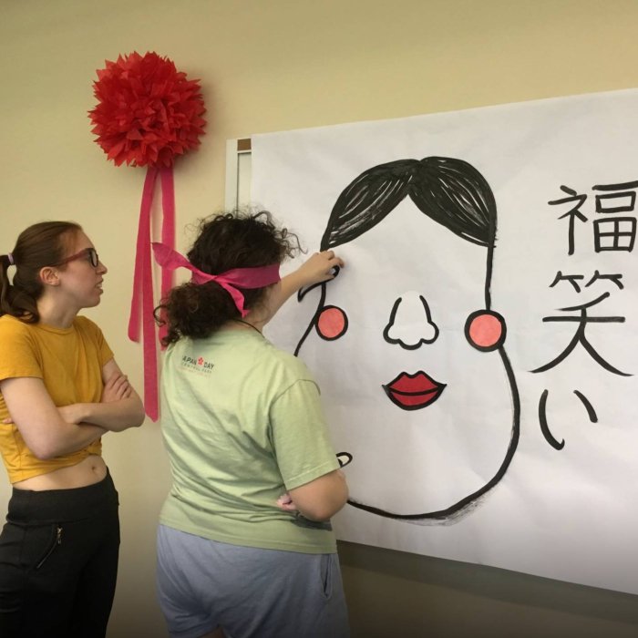 A college student watches as another student is blindfolded and tries to pin something on a white paper on the wall